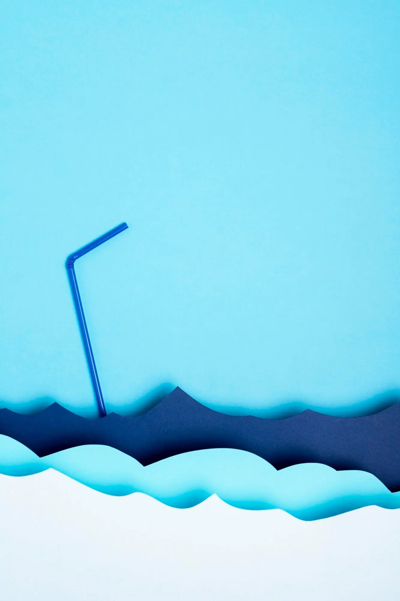 Draufsicht auf aus Papier gestaltete Meereswellen mit einem Plastikstrohhalm.